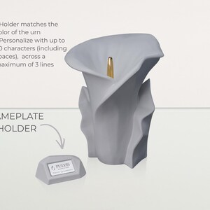 May include: A gray, calla lily-shaped urn with a gold accent. A small, gray nameplate holder is next to the urn. The text on the image says "NAMEPLATE HOLDER" and "PULVIS". The urn can be personalized with up to 50 characters.