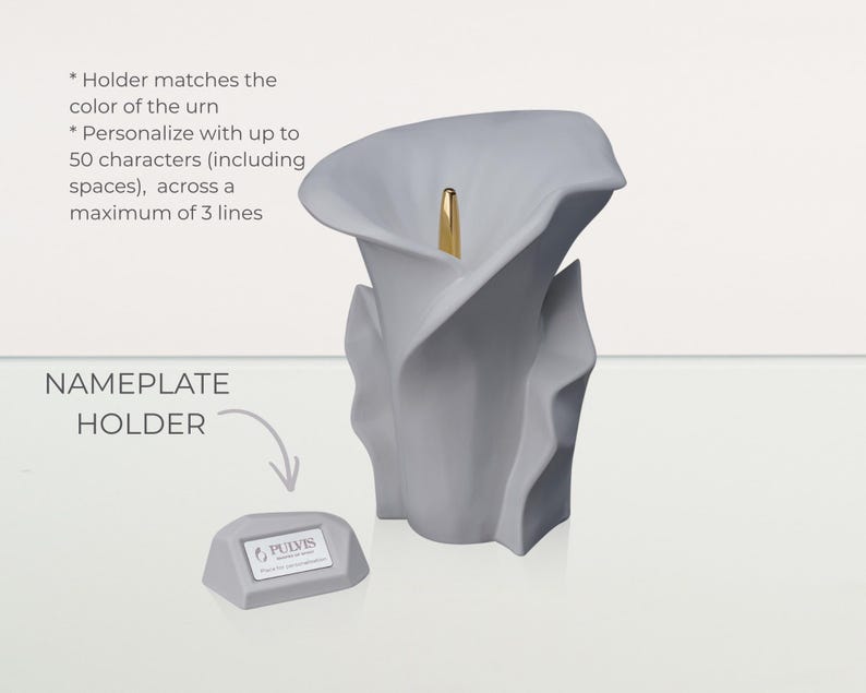 May include: A gray, calla lily-shaped urn with a gold accent. A small, gray nameplate holder is next to the urn. The text on the image says "NAMEPLATE HOLDER" and "PULVIS". The urn can be personalized with up to 50 characters.