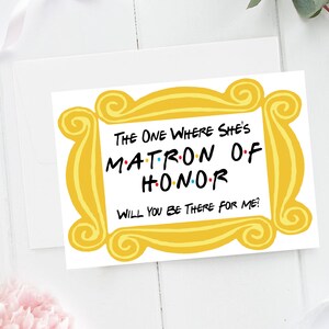 Puede incluir: Una tarjeta amarilla con un marco dorado alrededor de los bordes. El texto dentro del marco dice "The One Where She's Matron of Honor. Will You Be There For Me?"