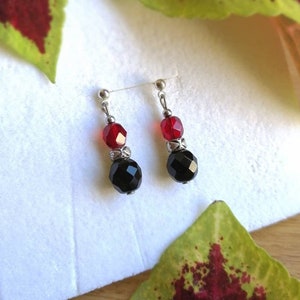 Könnte beinhalten: Ein Paar Ohrringe mit schwarzen und roten facettierten Glasperlen. Die Ohrringe sind silberfarben und haben ein schlichtes Design.