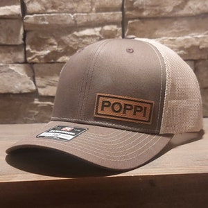 May include: A brown and beige trucker hat with a brown leather patch that says "POPPI" on it.