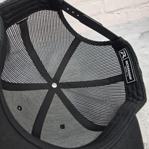 May include: Black trucker hat with a mesh back and a snapback closure. The interior features a structured crown and a mesh lining for breathability. The Richardson Model 112 label is visible on the inside.