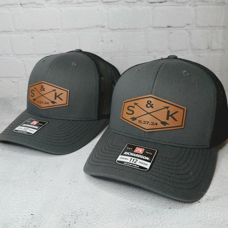 May include: Two gray and black trucker hats with a brown leather patch featuring the initials "S & K" and the date "11.27.24".