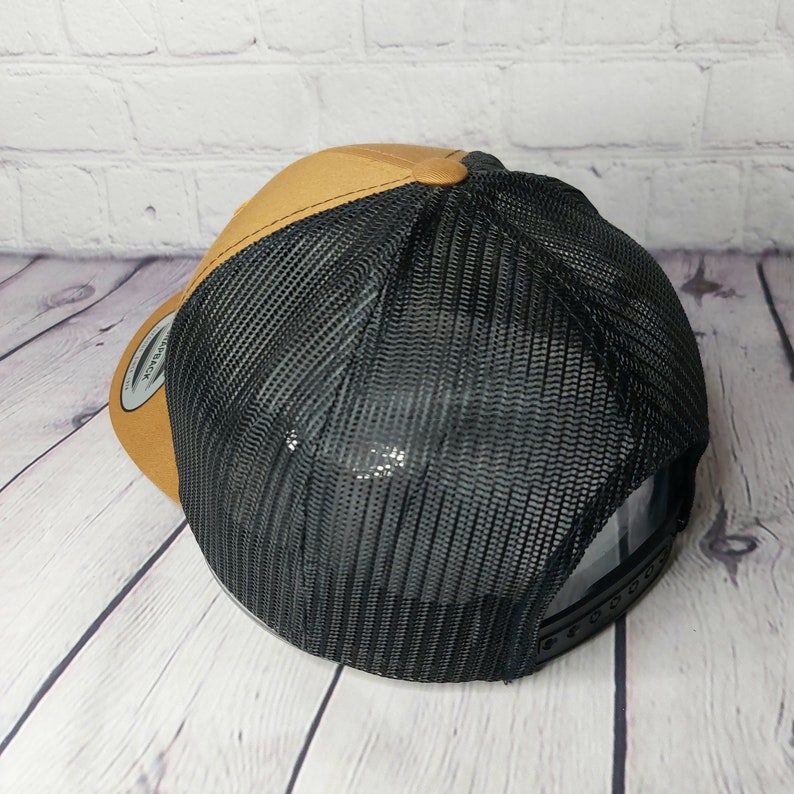 May include: A trucker hat with a brown front panel and a black mesh back. The hat has a curved brim and a snapback closure. The hat is made of a durable material and is designed for comfort and style.