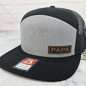 May include: Black and gray flat bill snapback hat with a mesh back. The front panel is gray with a brown leather patch that reads "PAPA". A Richardson tag is on the brim.