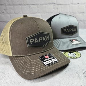 May include: Two brown and gray trucker hats with a black patch that says "PApaw" on each. The hats are both adjustable and have a mesh back.