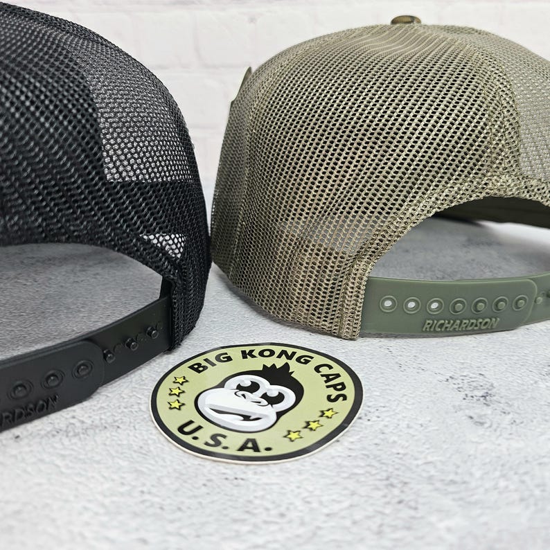May include: Two trucker hats with mesh backs. One hat is black, the other is olive green. The adjustable straps are black and olive green. A sticker with a monkey graphic and the text "BIG KONG CAPS U.S.A." is in the foreground.