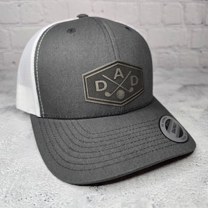 May include: A gray and white trucker hat with a black and white embroidered patch that says "DAD" with crossed golf clubs and a golf ball.