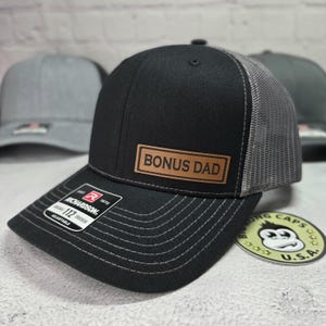 May include: Black and gray trucker hat with a brown leather patch that says "Bonus Dad".