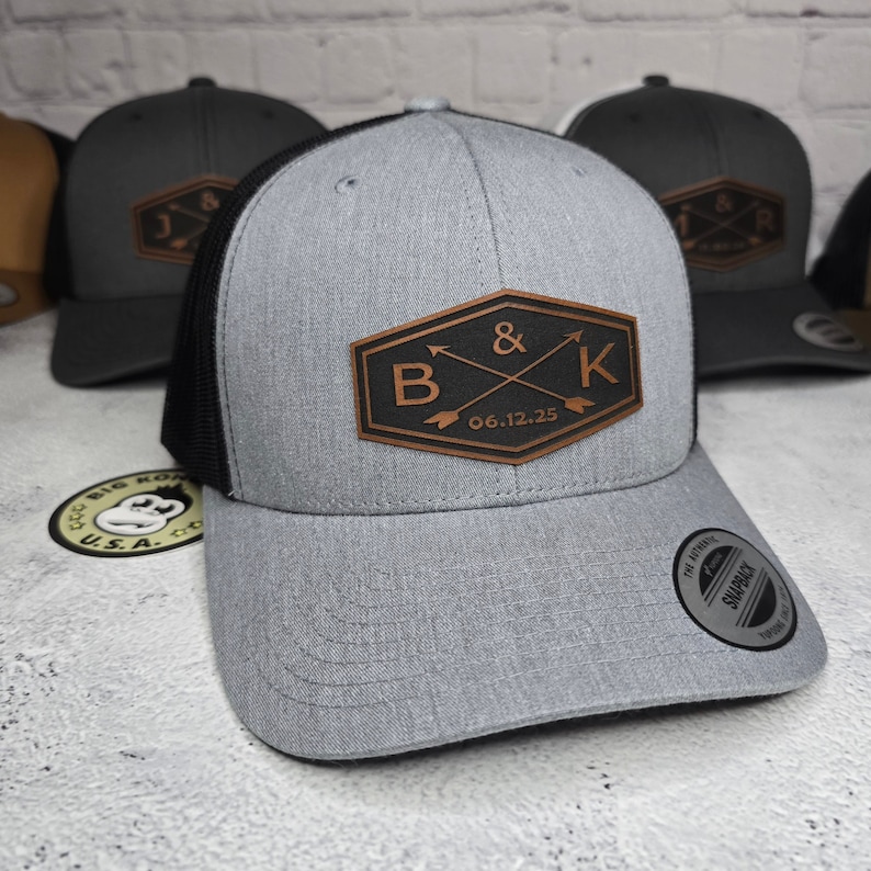 May include: A gray and black trucker hat with a brown leather patch that says "B & K 06.12.25".