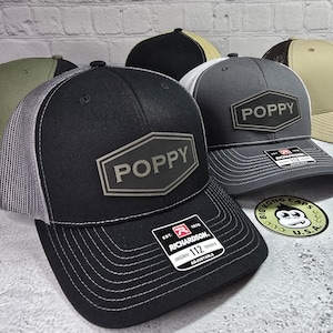 May include: Black, gray, and khaki trucker hats with a gray patch that says "POPPY" on the front. The hats are adjustable and have a mesh back.