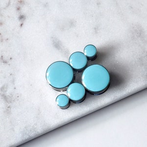 May include: A cluster of six light blue round ceramic tiles with silver rims, arranged in a random pattern.