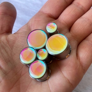 May include: A set of six iridescent ear gauges in various sizes. The gauges are made of stainless steel and have a smooth, polished finish. The iridescent finish creates a rainbow effect that changes with the light.