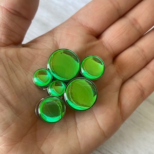 May include: A set of six green iridescent glass ear gauges of varying sizes. The gauges are round and have a shiny, reflective surface.