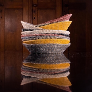 May include: A stack of woven bowls in various shades of blue, yellow, and red. The bowls are made of a natural material and have a rustic, handmade look.