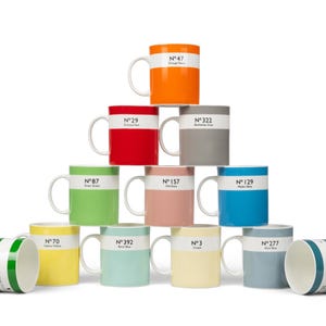 May include: A selection of brightly coloured ceramic mugs, each with a white band and a colour name and number. The mugs are arranged in a pyramid. Colours include orange, red, grey, green, pink, blue, yellow, teal, cream, and a darker blue.