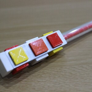 May include: A white plastic device with three colored buttons. The buttons are red, orange, and yellow. The device is attached to a clear plastic tube.
