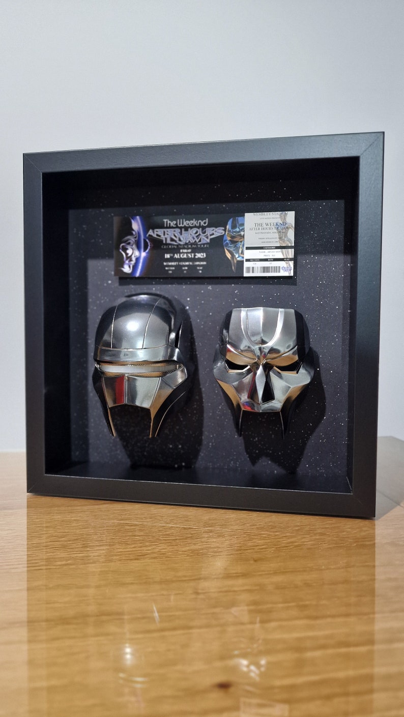 May include: A black framed shadow box with two silver masks and a concert ticket for The Weeknd's After Hours Til Dawn tour. The ticket is for the August 18, 2023 show at Wembley Stadium.