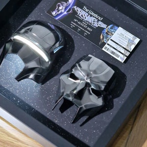 May include: A black framed shadow box with two black masks and a concert ticket for The Weeknd's After Hours Tour on August 18, 2023 at Wembley Stadium in London.