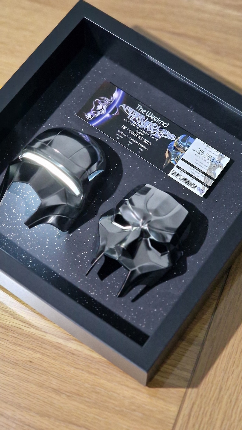 May include: A black framed shadow box with two black masks and a concert ticket for The Weeknd's After Hours Tour on August 18, 2023 at Wembley Stadium in London.