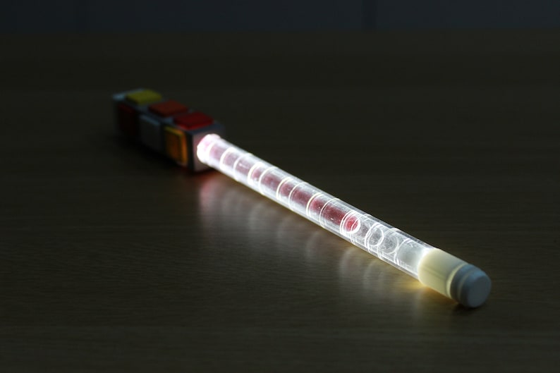 May include: A clear plastic tube with red and white accents, lit from within, creating a bright white glow. The tube is attached to a colorful block with red, yellow, and white squares.