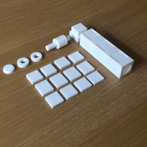 May include: A set of white plastic building blocks, including a long rectangular piece, a small square piece, and several round pieces. The blocks are arranged on a wooden surface.