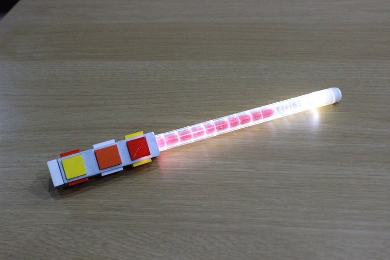 May include: A white plastic tube with a red light inside. The tube is attached to a white base with three colored buttons: yellow, orange, and red.