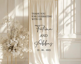 May include: A cream-colored wedding welcome sign with gold frame. The sign reads "THANK YOU FOR CELEBRATING WITH US!" followed by the names "Fatima AND Abbas" and the date "19.06.2025". A floral arrangement is on the left.