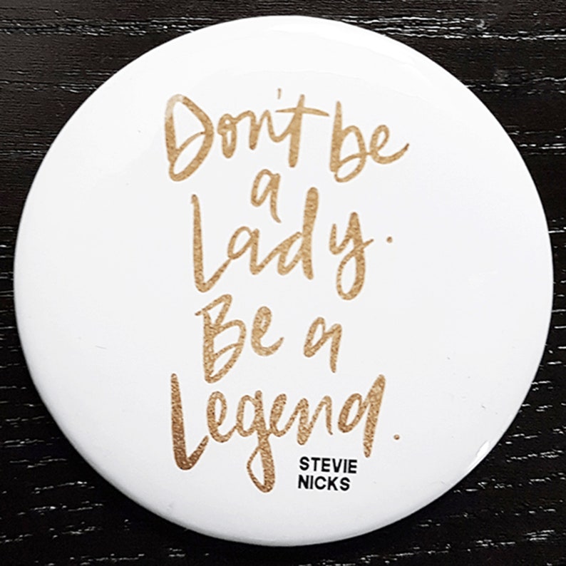 Pu&ograve; includere: Bottone rotondo bianco con scritta dorata "Don't be a lady. Be a legend." con il testo "Stevie Nicks" in lettere pi&ugrave; piccole sotto.