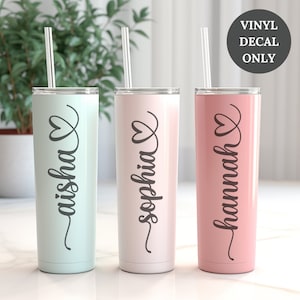 May include: Three stainless steel tumblers with vinyl decals. The tumblers are in different colors: light blue, white, and pink. Each tumbler has a heart and a name on it: "Aisha", "Sophia", and "Hannah".