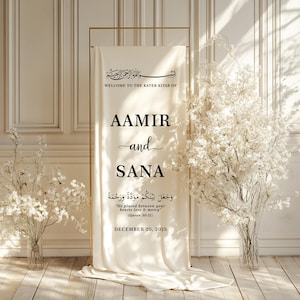 Peut inclure: Une banni&egrave;re de mariage cr&egrave;me avec un cadre dor&eacute;, affichant les noms "AAMIR and SANA" dans une &eacute;criture &eacute;l&eacute;gante. La banni&egrave;re comprend de la calligraphie arabe et la date "DECEMBER 20, 2025". Des arrangements floraux blancs encadrent la banni&egrave;re.