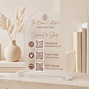 Peut inclure: Un panneau en acrylique dépoli en forme d'arche avec du texte brun et trois codes QR. Le panneau affiche "The Bloom Collective", "Connect & Shop" et des identifiants de réseaux sociaux. Il inclut des icônes Instagram, Venmo et un site web.