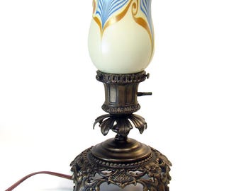 May include: A vintage table lamp with a white glass shade with blue and gold swirls. The lamp has a bronze base with an ornate design.