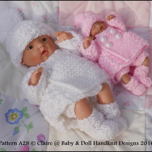 Könnte beinhalten: Zwei gestrickte Puppenoutfits, eines weiß und eines rosa, mit passenden Mützen. Die Outfits sind mit Perlenknöpfen verziert und für eine kleine Puppe konzipiert.