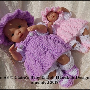 May include: Two knitted doll outfits in pink and purple with white accents. The outfits include dresses, bonnets, and booties. The pattern is called "Claire's Baby & Doll Handknit Designs 2008, amended 2018."