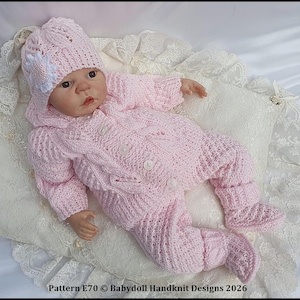 May include: A light pink hand-knitted baby outfit consisting of a long-sleeved button-up cardigan, matching trousers, and a beanie with a white flower accent. The set features a textured cable knit pattern. Text reads: Pattern E70 © Babydoll Handknit Designs 2026.