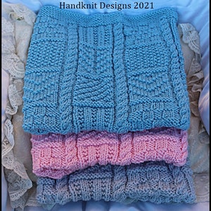 May include: Three knitted baby blankets in blue, pink, and gray. The blankets are stacked on top of each other. The top blanket is blue, the middle blanket is pink, and the bottom blanket is gray. The blankets are all made with a cable knit stitch. The text "Pattern H24 © Claire's Baby & Doll Handknit Designs 2021" is visible at the top of the image.