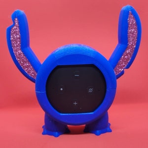 Peut inclure: Coque 3D imprimée en bleu et rose pour un haut-parleur intelligent, en forme de personnage de dessin animé avec de grandes oreilles. Le haut-parleur a des boutons pour le volume, la lecture/pause et la désactivation du microphone.