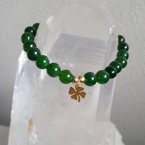 May include: A green jade stone bracelet with a gold four-leaf clover charm.