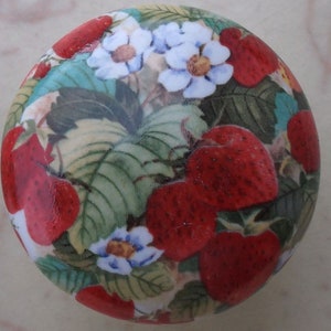 May include: A round ceramic knob with a colorful floral pattern featuring red strawberries, white flowers, and green leaves.