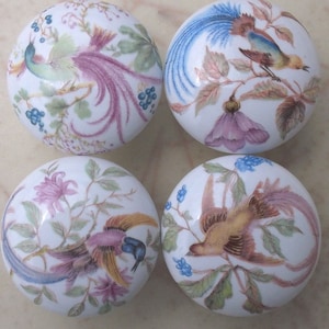 May include: Four white ceramic knobs with a floral design and colorful birds. Each knob features a different bird with a long tail and intricate details.