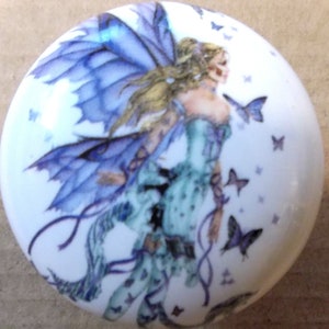 May include: A white ceramic knob with a purple fairy with wings and a blue dress surrounded by butterflies.