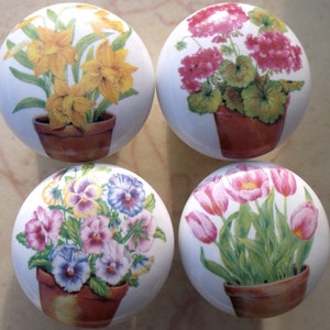 May include: Four ceramic knobs with floral designs. Each knob features a different flower in a pot: daffodils, geraniums, pansies, and tulips.