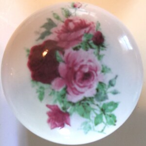 May include: A white ceramic knob with a floral design featuring pink and burgundy roses with green leaves.
