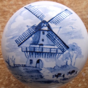 May include: A white ceramic knob with a blue and white windmill design. The windmill has a white base and blue blades.