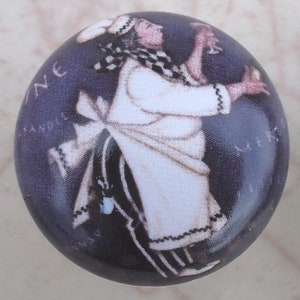 May include: A round, decorative cabinet knob with a dark blue background. The knob features a vintage illustration of a person in a white chef's outfit holding a glass. The text "Wine Sample" is visible on the knob.