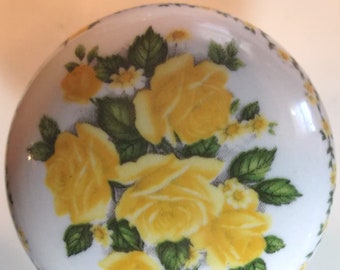 May include: A white ceramic knob with a yellow rose floral design. The knob has a raised edge and a smooth surface.
