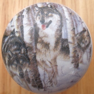 May include: A white round ornament with a printed image of a wolf in a forest setting. The wolf is brown and white and has a pink tongue sticking out.