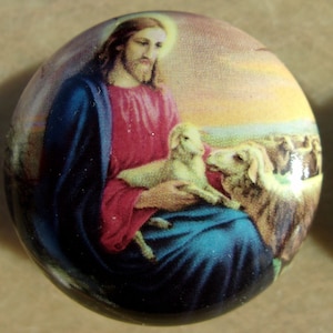 May include: A round, colorful image of Jesus holding two white lambs. The background is a sunset with a field of grass.