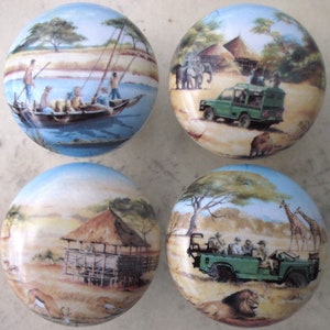 May include: Set of four ceramic knobs featuring safari scenes. Each knob depicts a different scene, including a boat on a river, a jeep driving through the savanna, a hut in the bush, and a jeep with passengers driving past a lion and giraffes. The knobs are painted in a realistic style with vibrant colors.